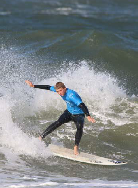 Ein Mann in einem blauen Hemd reitet auf einem Surfbrett auf einer Welle.